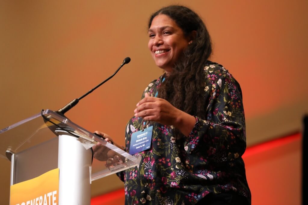 A woman at a podium is smiling and gesturing