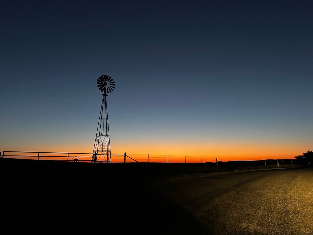 The silhouette of a fence line and windmill at sunset